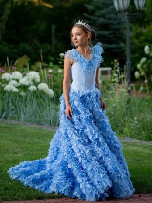 Daisy gown in light blue with feather-like embellishments, cascading ruffles, and tiara—styled outdoors in a garden setting for weddings, fantasy photoshoots, and royal-themed celebrations.