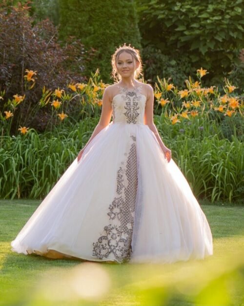Elisabeth white ball gown with black embroidery, voluminous tulle skirt, and crown—styled outdoors in a garden with blooming lilies for weddings, fantasy shoots, and royal-themed celebrations.
