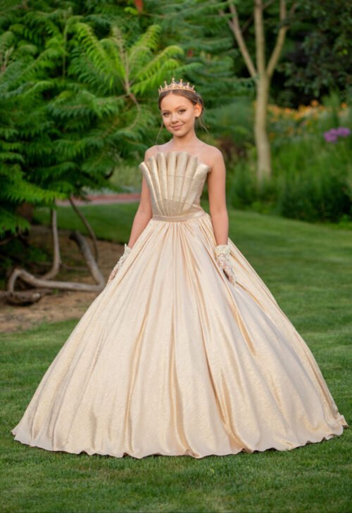 Grace gown for girls in champagne with seashell bodice, voluminous skirt, golden crown, and gloves—styled in garden setting for weddings, pageants, and royal-themed celebrations.