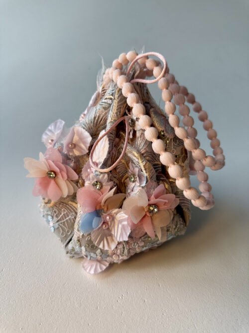 Ornate pastel drawstring pouch with floral embellishments, lace embroidery, and pom-pom handle.