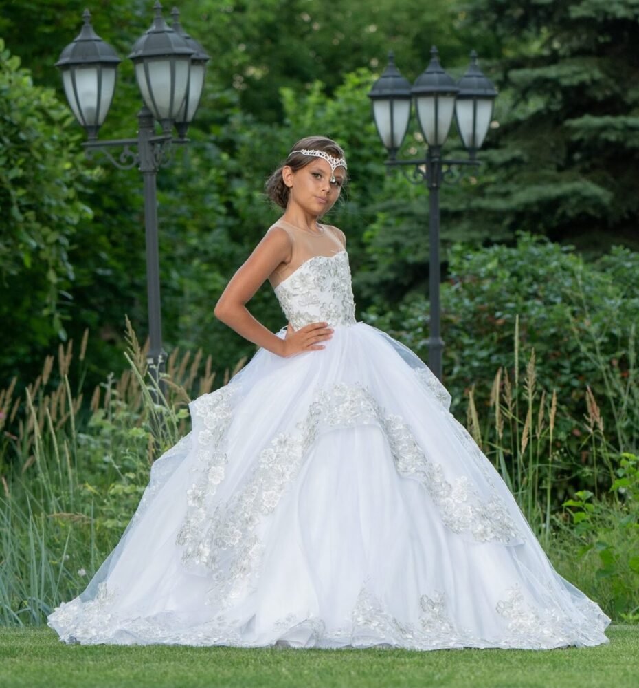 Layla white ball gown with silver floral embellishments, lace detailing, and thin straps—styled outdoors in a garden with hydrangeas and lantern posts for weddings, fantasy shoots, and royal-themed celebrations.