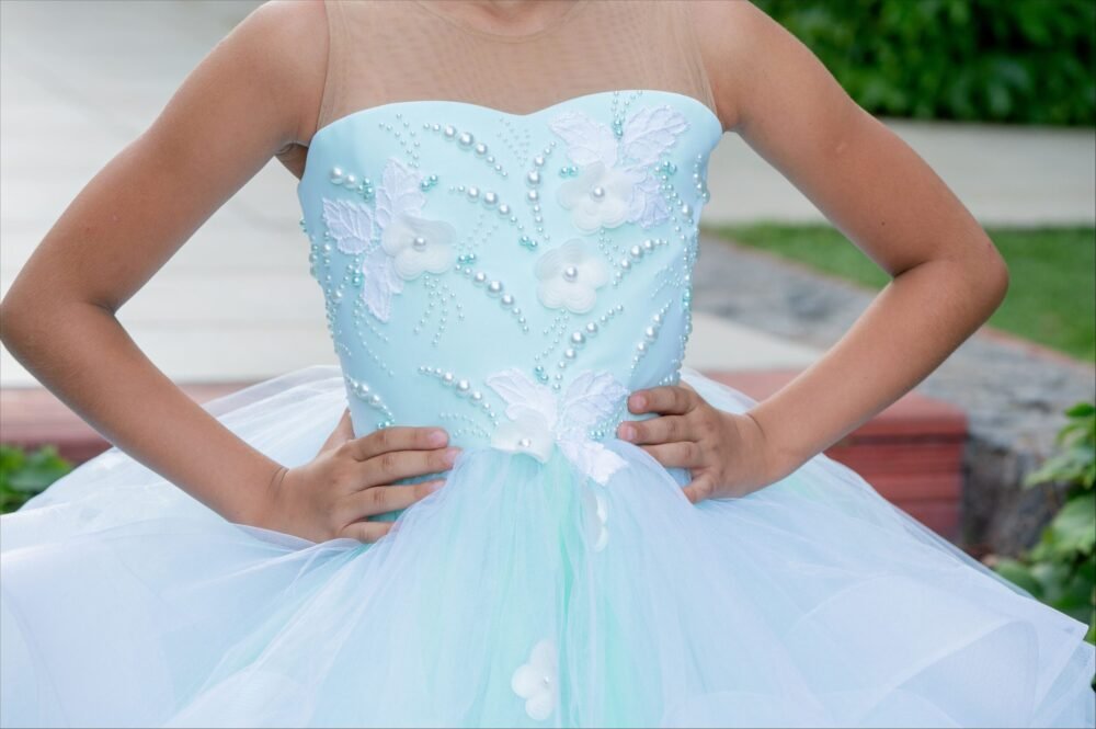Close-up of Olivia light blue strapless ball gown with white floral appliqués, butterfly motifs, pearl beadwork, and layered tulle skirt—styled outdoors for weddings, fantasy shoots, and royal-themed celebrations.