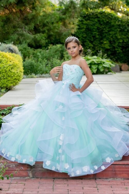 Olivia light blue ball gown with layered tulle skirt, floral hem embellishments, and sequin bodice—styled outdoors in a garden setting with tiara for weddings, fantasy shoots, and royal-themed celebrations.