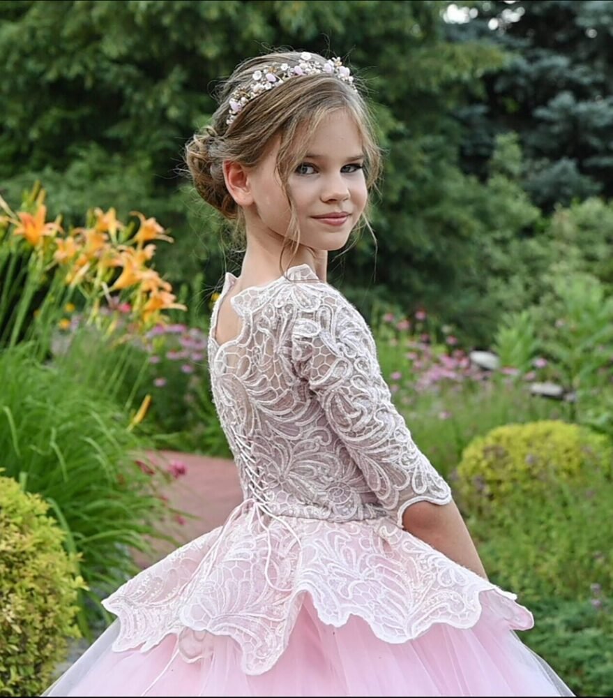 Back view of Rosie light pink ball gown with floral lace bodice, peplum waist, and layered tulle skirt—styled outdoors in a garden with orange lilies for weddings, fantasy shoots, and royal-themed celebrations.