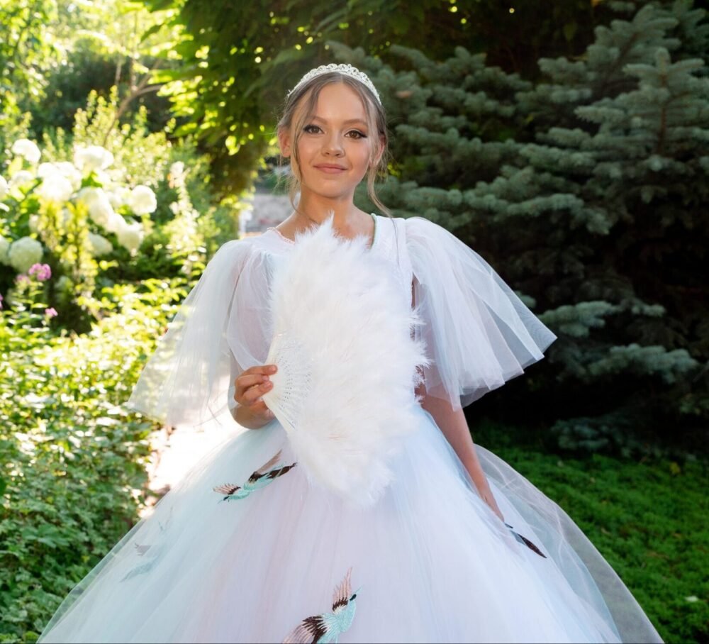 Sophia white ball gown with puff sleeves, bird appliqués, and layered tulle skirt—styled outdoors in a garden with tiara and feathered fan for weddings, fantasy shoots, and royal-themed celebrations.