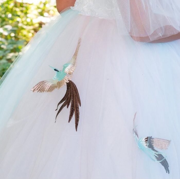 Close-up of Sophia gown embroidery showing two birds in flight with detailed feathers on white tulle—nature-inspired embellishment for couture gowns, fantasy shoots, and garden-themed celebrations.