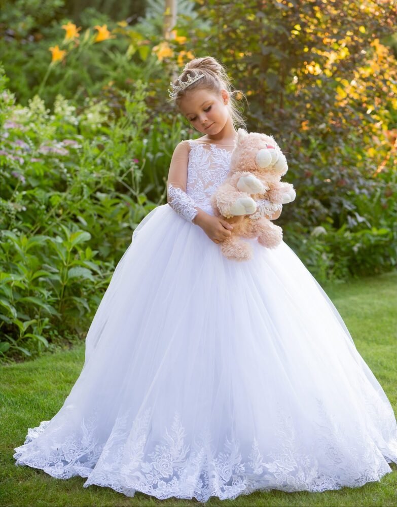 THEA white ball gown with lace bodice, full tulle skirt, tiara, and plush teddy bear—styled outdoors on a grassy lawn with blooming flowers for weddings, fantasy shoots, and royal-themed celebrations.