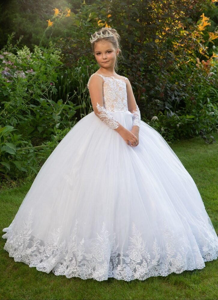 THEA white ball gown with lace bodice and sleeves, full tulle skirt, and crown—styled outdoors in a sunlit garden with blooming flowers for weddings, fantasy shoots, and royal-themed celebrations.