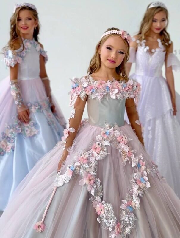 Three girls wearing pastel ball gowns with floral appliqués, puff sleeves, and headbands in an editorial setting